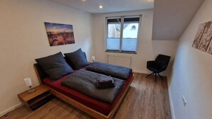 Ein Schlafzimmer mit einem Bett, einem Nachttisch, einem Sessel und einem Fenster.