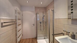 Ein modernes Badezimmer mit einer gläsernen Duschkabine, einem weißen Waschbecken und einem Handtuchhalter.