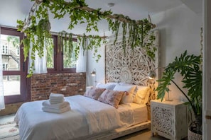 Une chambre à coucher avec un lit, une tête de lit blanche, un mur en briques et une fenêtre.