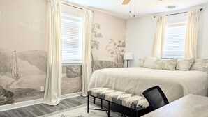 Een slaapkamer met een bed, een bankje, een bureau en een lamp.