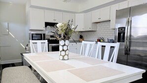 Een moderne keuken met witte kasten, een roestvrijstalen koelkast, een magnetron en een eettafel met placemats.