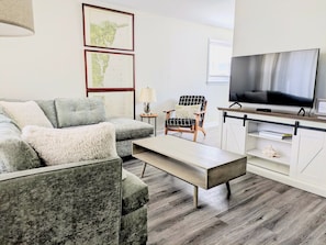A modern living room with a grey sofa, a coffee table, a TV, and a bookshelf.