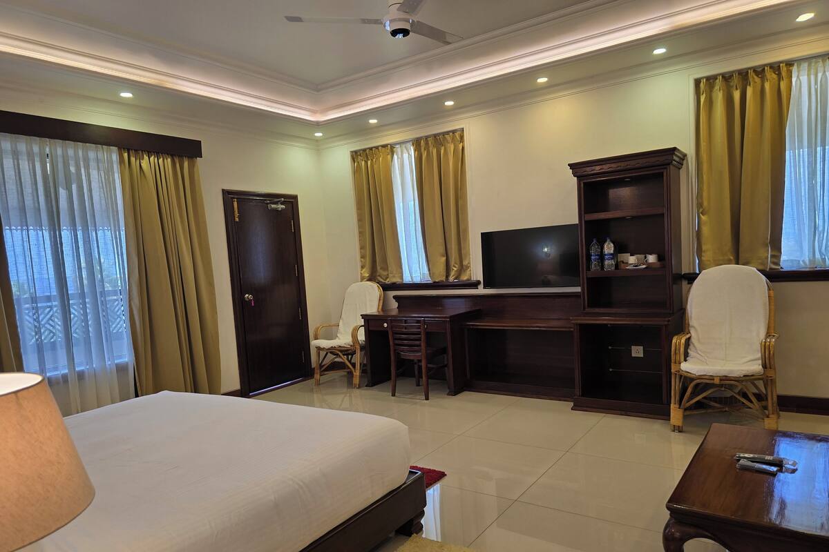A hotel room with a bed, desk, chair, TV, and a small table.