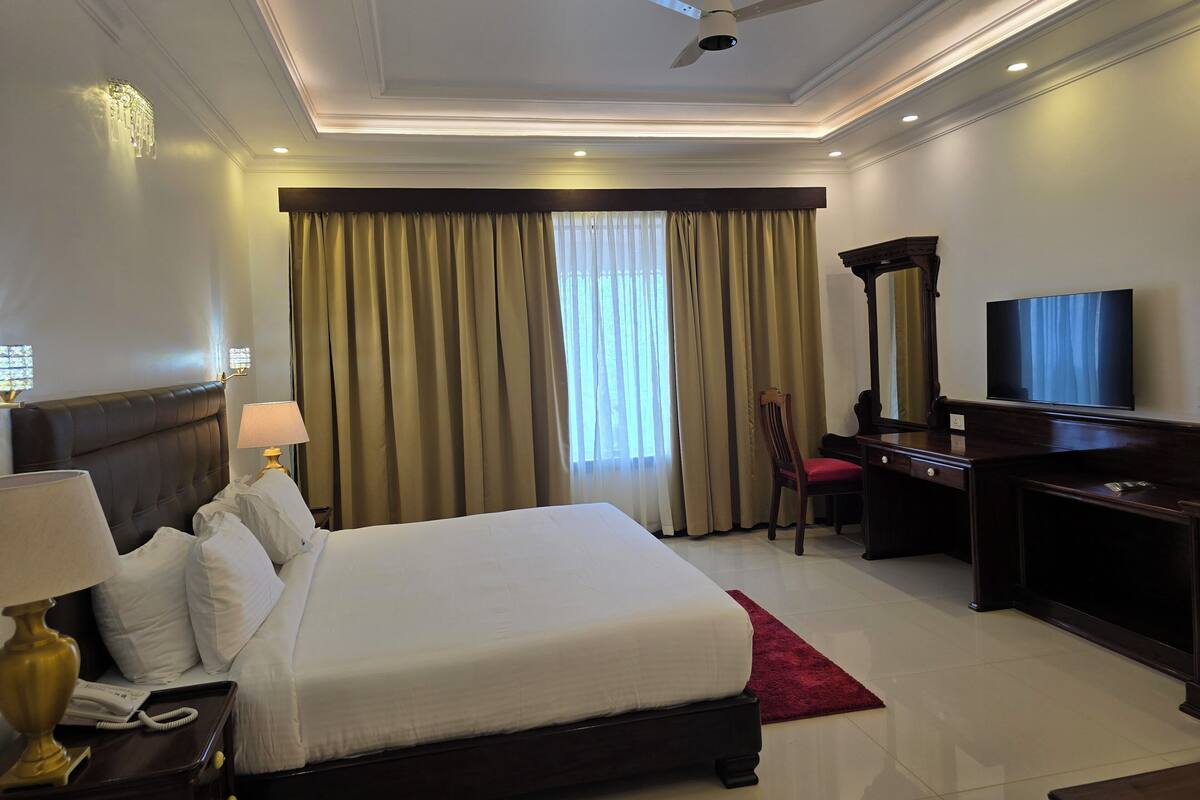 A hotel room with a large bed, a desk, a chair, a television, and a ceiling fan.
