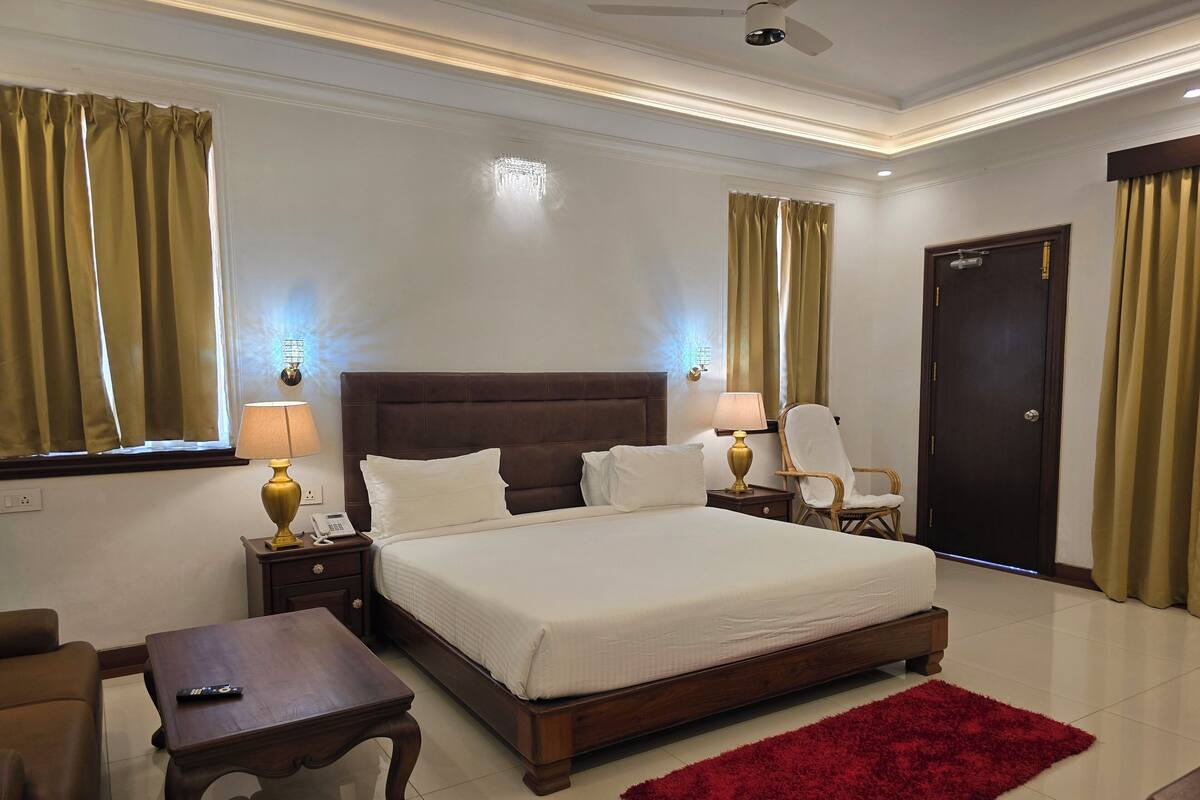 A hotel room with a large bed, two bedside tables with lamps, a wooden chair, a red rug, and a door.