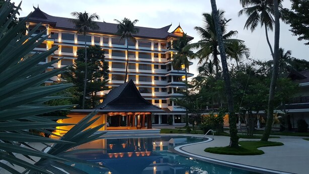 Ein mehrstöckiges Hotel mit Swimmingpool, umgeben von Palmen und gut beleuchteten Außenbereichen.