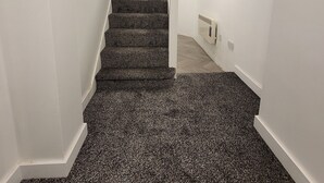 A staircase with carpeted steps leading to a landing with a light switch and a power outlet.