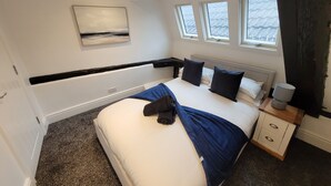 A bedroom with a bed, a nightstand, a lamp, a window, and a painting on the wall.