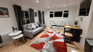 A modern living room with a grey sofa, a small round table, and a dining area with a wooden table and chairs.