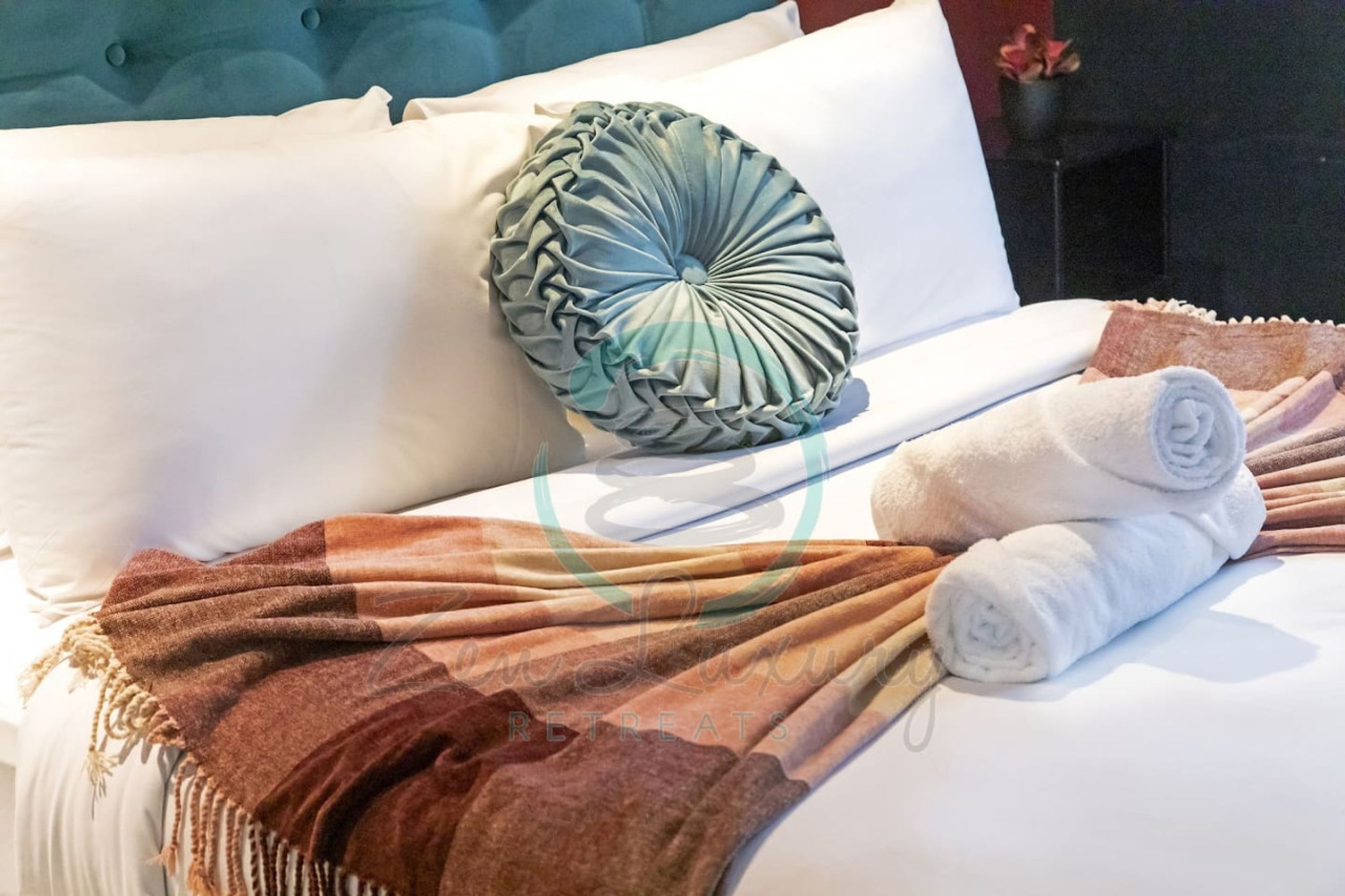 A neatly made bed with white linens, a brown throw blanket, and a decorative pillow.