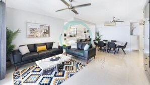 Ein modernes Wohnzimmer mit einer schwarzen Couch, einem Couchtisch und einem Essbereich mit einem weißen Tisch und Stühlen.