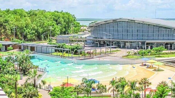 Ein Resort mit großem Schwimmbad, Strandbereich und einem modernen Gebäude mit gewölbtem Dach.