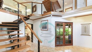 Un intérieur spacieux avec un escalier en bois, une grande porte donnant sur l’extérieur et un sol carrelé.