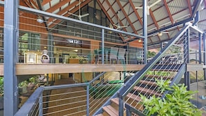 Un bâtiment à plusieurs niveaux doté d’une terrasse en bois, de rampes en métal et d’un escalier.