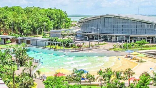 A large swimming pool with a surrounding deck, a covered area, and a view of a stadium in the background. - Zenhouse Stylish Lawn Workspace Outdoordining (Muirhead)