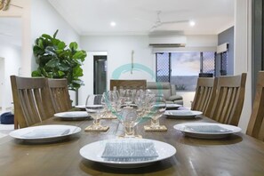 A dining table set for six with clear glassware and plates, surrounded by wooden chairs.