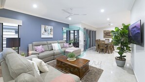 A modern living room with a sofa, coffee table, and a dining area with chairs and a TV. - Zenhouse Stylish Lawn Workspace Outdoordining (Muirhead)