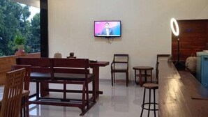 Une pièce spacieuse avec un banc en bois servant de coin salon, une petite table et un comptoir de bar avec des tabourets. Un téléviseur à écran plat est fixé au mur.