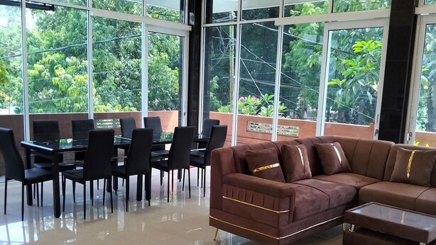 Une pièce spacieuse avec de grandes fenêtres, un canapé marron, une table à manger avec des chaises et un sol carrelé réfléchissant.
