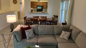 Una sala de estar con un sofá modular, una mesa de comedor y una cocina al fondo.