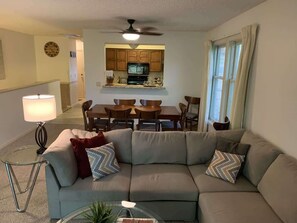 A living room with a sectional sofa, a dining table, and a kitchen in the background.