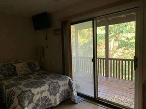 A bedroom with a bed, a television mounted on the wall, and a sliding glass door leading to an outdoor deck.