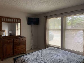 A bedroom with a bed, a dresser, a television, and large windows.