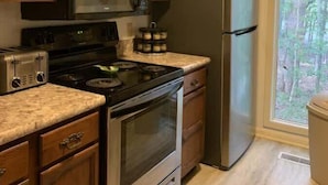 Una cocina con armarios de madera, un refrigerador de acero inoxidable, un microondas, una estufa y una ventana con vista a árboles.