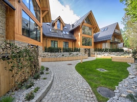 Una casa moderna con fachada de piedra, detalles de madera y un sendero de piedra que conduce a una zona verde.