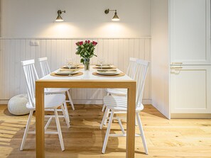 A dining area with a wooden table set for four, surrounded by white chairs, with a vase of flowers in the center.