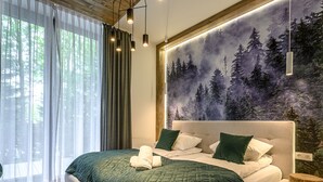 A modern bedroom with a large bed, a forest-themed wall mural, and a wooden floor.