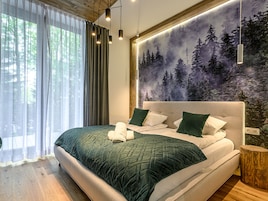 Un dormitorio moderno con una cama grande, un mural temático de bosque y piso de madera.