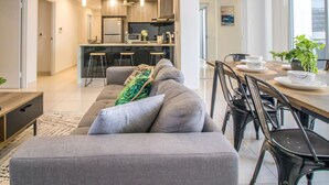 Un salon moderne avec un canapé gris, une table à manger et des chaises, et une cuisine en arrière-plan.
