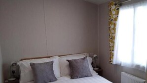 Une chambre à coucher comprenant un lit, deux tables de chevet, une commode, une fenêtre avec des rideaux et un luminaire au plafond.
