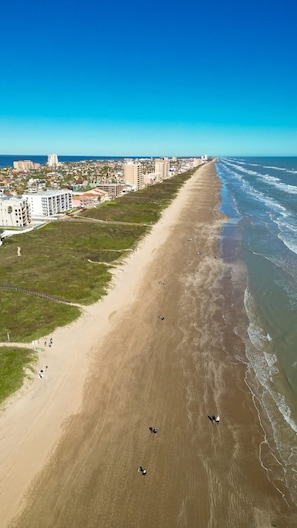 An aerial view of a beach with a clear sky, buildings in the background, and a few people on the sand. - Los Cabos Ii #4 2 Bedroom Condo by RedAwning (South Padre Island)
