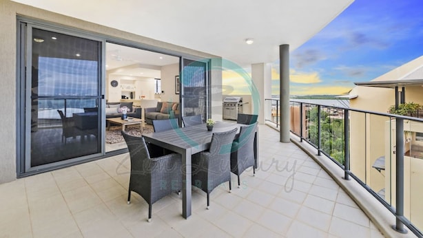 A balcony with a dining table and chairs, a sliding glass door leading to an interior space, and a view of the sky and landscape. - Lush Waterfront Charm Ocean Views Pool Office (Darwin)