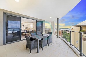 A balcony with a dining table and chairs, a sliding glass door leading to an interior space, and a view of the sky and landscape. - Lush Waterfront Charm Ocean Views Pool Office (Darwin)