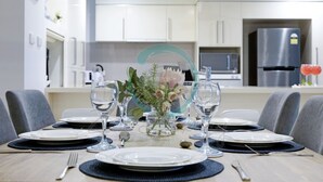 A dining area with a table set for four, including plates, glasses, and cutlery. - Lush Waterfront Charm Ocean Views Pool Office (Darwin)