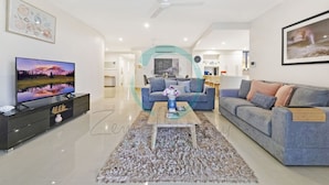 A modern living room with a flat-screen TV, two sofas, a coffee table, and a decorative archway. - Lush Waterfront Charm Ocean Views Pool Office (Darwin)