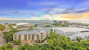 A modern building complex with multiple structures, including a large curved building and several rectangular buildings with flat roofs. - Lush Waterfront Charm Ocean Views Pool Office (Darwin)