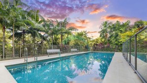 A swimming pool with a bench, surrounded by palm trees and a fence. - Lush Waterfront Charm Ocean Views Pool Office (Darwin)