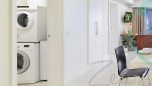 Ein modernes Wohnzimmer mit Essbereich, einem an der Wand montierten Fernseher und einer Waschmaschine im Hintergrund.