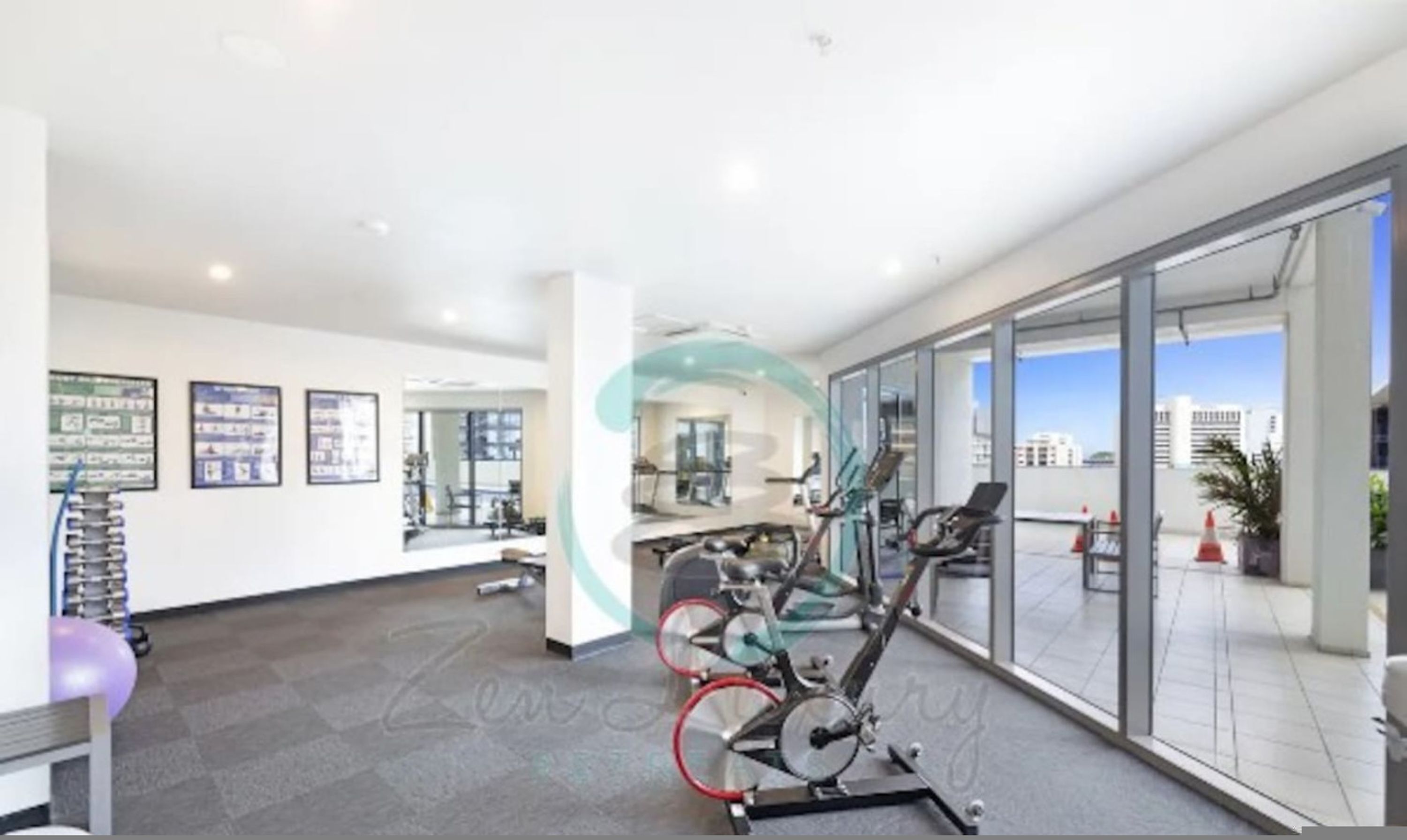 A gym with exercise equipment, a reception area, and large windows offering a view of the city.