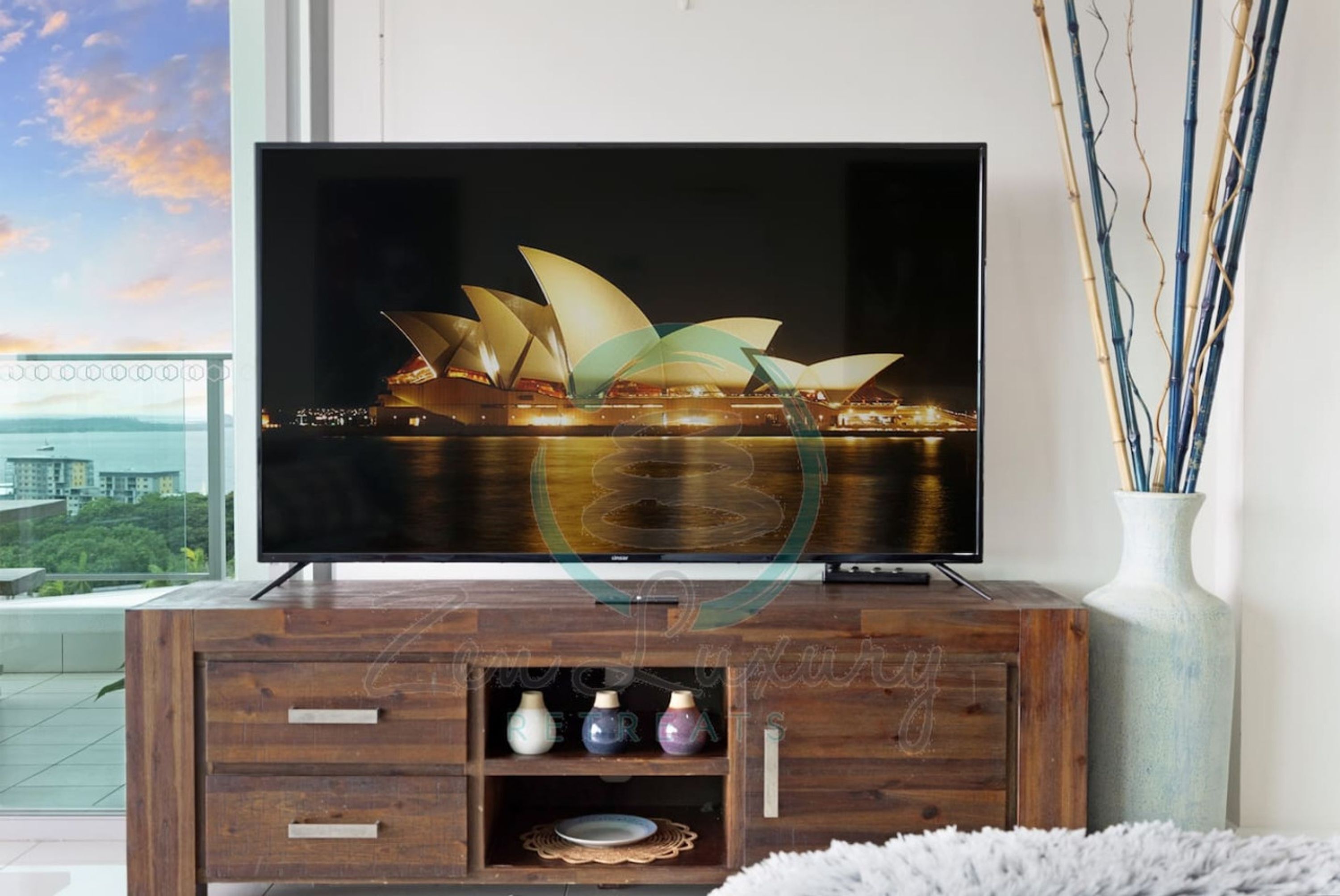 A flat-screen TV on a wooden cabinet with a view of the Sydney Opera House.