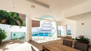 A spacious outdoor area with a wooden table and chairs, surrounded by potted plants and a view of the ocean. - Zen Skytower Harbourview -exclusive 3br Family Apt (Darwin)