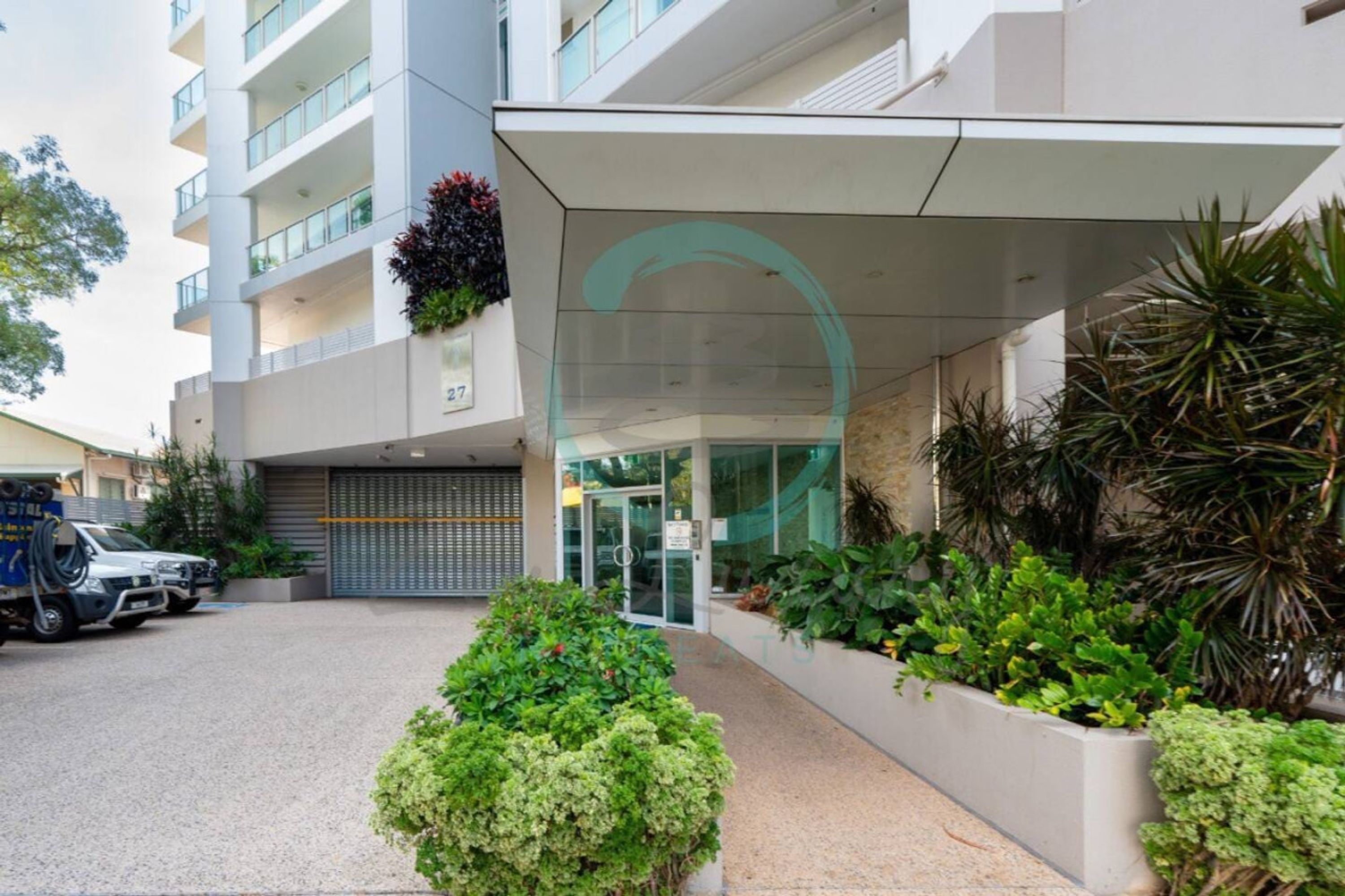 A modern building with a glass entrance, a parking area, and a well-maintained garden.