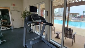 Esteira numa sala com uma janela grande com vista para uma área de piscina.