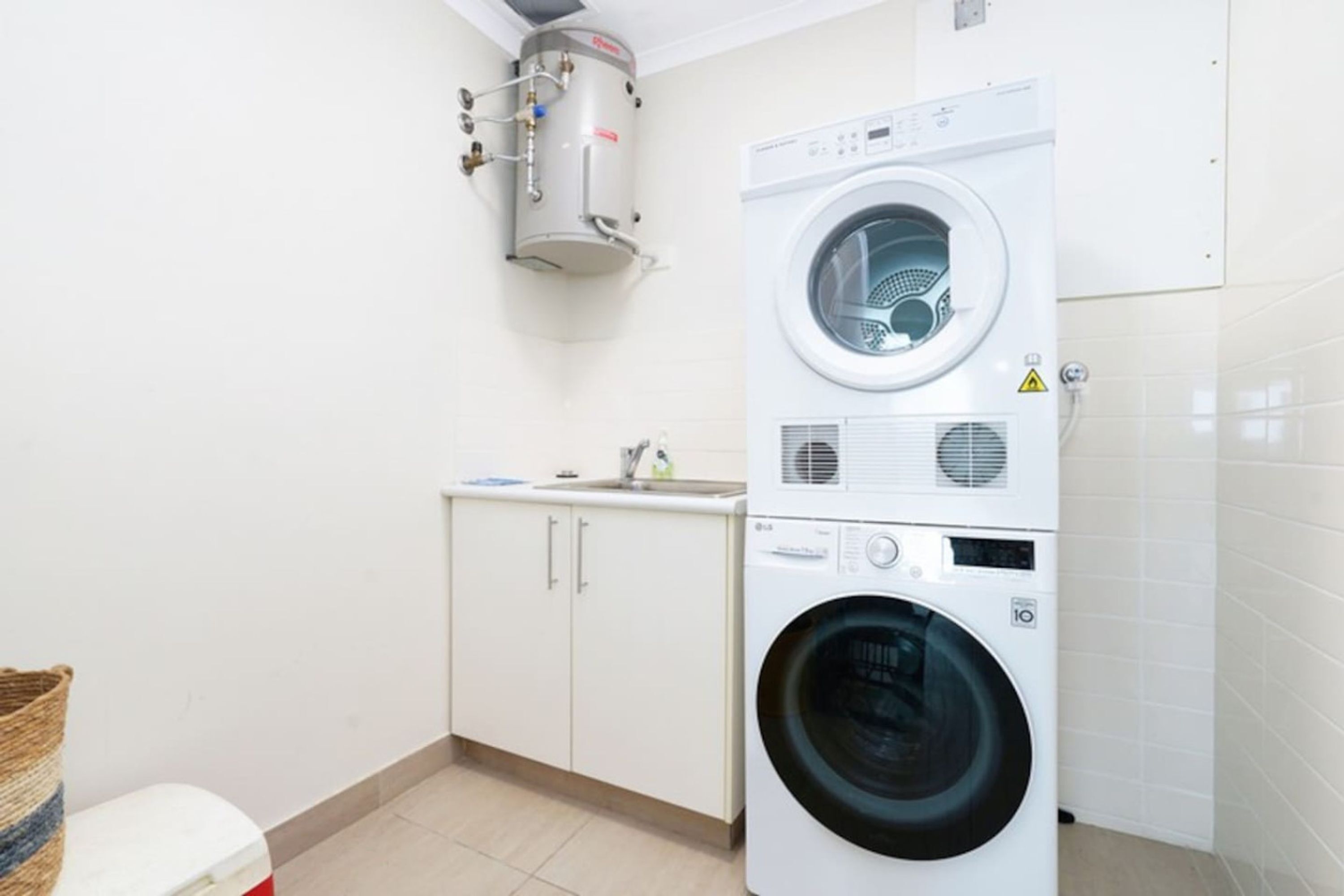 Uma lavanderia compacta com máquina de lavar e secadora empilhadas, aquecedor de água e uma pia pequena.