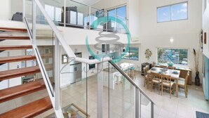 Ein modernes Interieur mit einer Treppe, die zu einer zweiten Etage führt, einem Essbereich mit Holzmöbeln und großen Fenstern mit Blick nach außen.