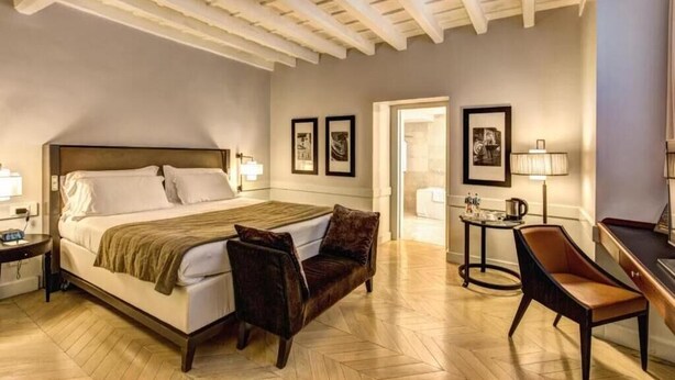 A hotel room with a bed, a desk, a chair, and a lamp.